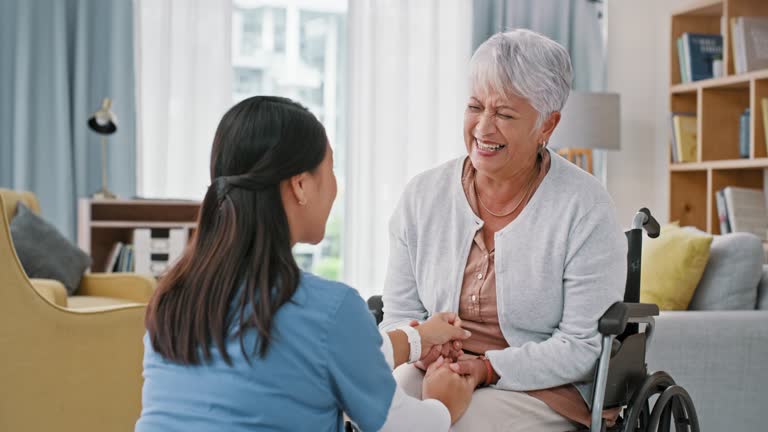Holding hands, nurse and talking to a senior woman in wheelchair with help or support. Elderly patient person with a disability laughing with happy caregiver for healthcare, kindness or medical care